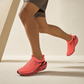 Orange air-cushion running shoe worn by a runner, cream studio backdrop
